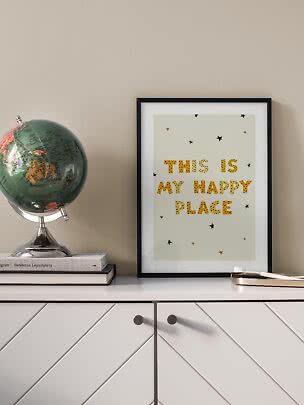 Gerahmtes Poster "This is my happy place" auf weißer Kommode neben einem Globus.