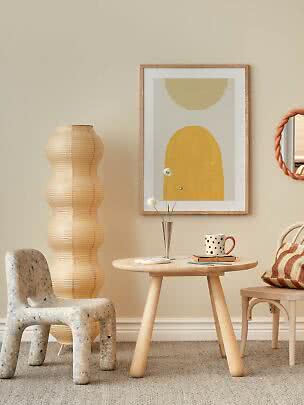 Gemütliche Ecke mit gelbem abstraktem Wandbild, rundem Holztisch, skulpturalem Stuhl und Stehlampe.