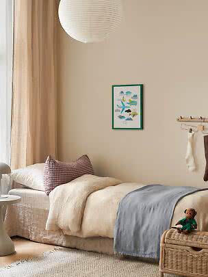 Accogliente cameretta con letto, biancheria beige, plaid blu, lampada di carta e baule in vimini