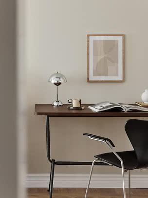 Minimalistischer Schreibtisch mit Chromlampe, Tasse, offenem Buch und gerahmter abstrakter Kunst