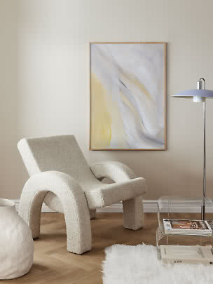 Moderne stuehjørne med cremefarvet lænestol, abstrakt vægkunst og gulvlampe