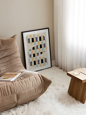Gerahmtes abstraktes Poster an der Wand neben beigem Sessel, weißem Teppich und Holztisch