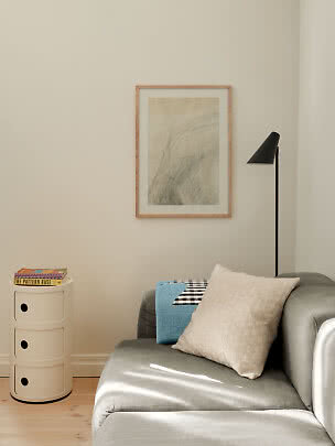 Ljust vardagsrumshörn med grå soffa, kuddar, svart golvlampa och litet vitt förvaringsskåp.
