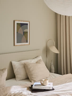 Camera da letto accogliente con letto neutro, cuscini, libro con tazza, lampada e arte astratta