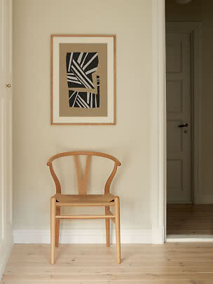Light wooden chair beneath framed abstract black-and-white print on a beige wall
