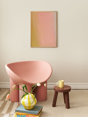 Rosa Sessel mit braunem Hocker, gelber Tasse und gestreifter Vase mit Tulpen unter abstraktem Bild