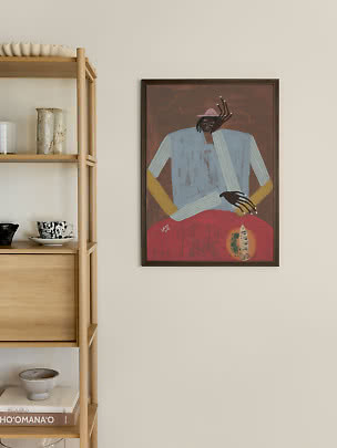 Gerahmter Kunstdruck einer sitzenden Figur in blauer Kleidung und rosa Hut an beiger Wand