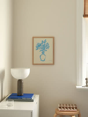 Affiche florale bleue encadrée sur mur beige au-dessus d'une commode avec lampe et livres