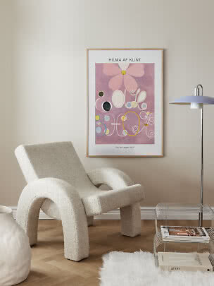 Indrammet Hilma af Klint-plakat med rosa abstrakt motiv på beige væg over en lænestol