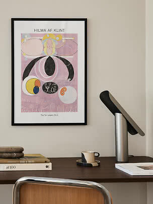 Ingelijste Hilma af Klint-poster met abstract motief in roze, geel en zwart boven een donker bureau