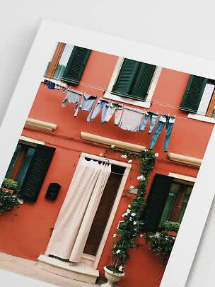 Angled photo of a red building with green shutters and laundry hanging on a line
