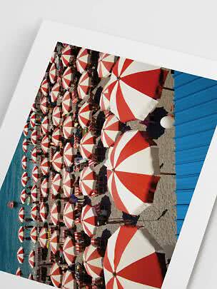 Photo of a beach with red and white umbrellas by the sea
