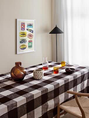 Spisebord med brunternet dug, glas og vase i lyst rum med sort gulvlampe.