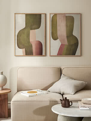 Deux affiches abstraites encadrées au-dessus d’un canapé beige, formes vertes, roses et brunes