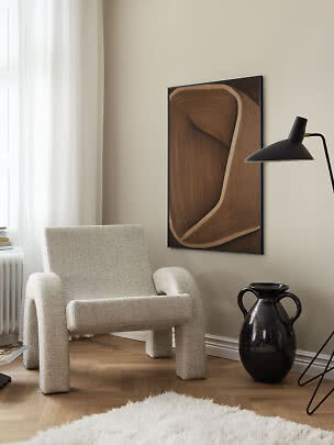 Fluffy cremefarvet lænestol i moderne stue med vægkunst, sort gulvlampe og mørk vase
