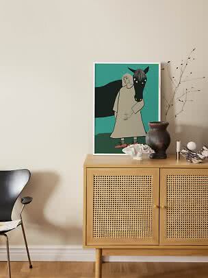 Illustration encadrée d’une femme avec un cheval noir sur fond turquoise, posée sur un buffet en bois