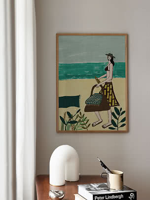 Framed art print of a woman on a beach with basket, sea and plants.