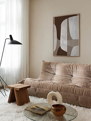 Beige rillet sofa i stue med abstrakt vægkunst, sort gulvlampe og glasbord