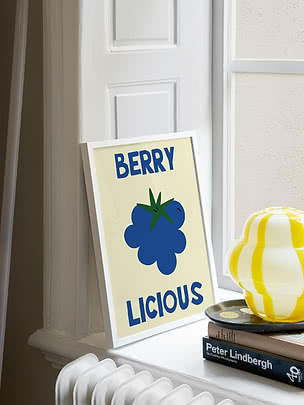 Indrammet plakat med blå bær og teksten "BERRY LICIOUS" på en hvid vindueskarm.