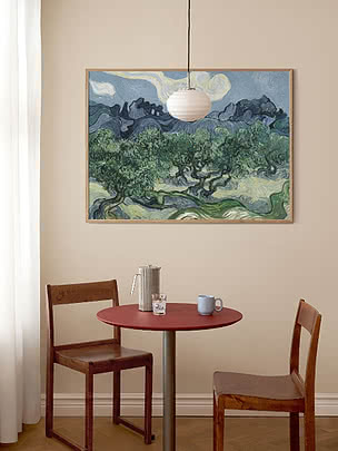 Dining nook with round red table, two wooden chairs, pendant light and large framed landscape painting