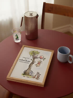 Ingelijste Winnie de Poeh-poster op rode tafel met kan, glas en mok