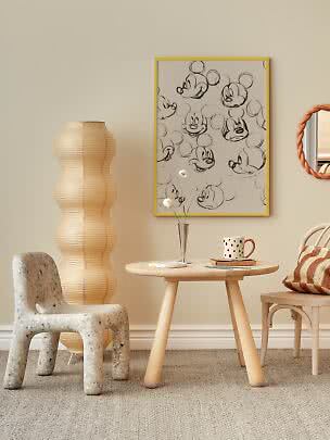 Poster mit skizzierten Mickey-Mouse-Gesichtern im gelben Rahmen an heller Wand