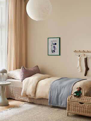 Accogliente cameretta con letto singolo, biancheria beige, lampada di carta e baule intrecciato