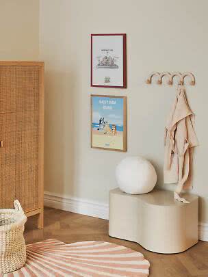 Kids room with beige wall hooks, robe, two posters and a wavy bench.