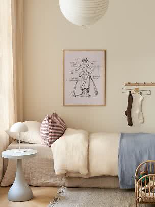 Gemütliches Kinderzimmer mit niedrigem Bett, weißer Tischlampe, Kissen, Wandbild und Papierlampe.