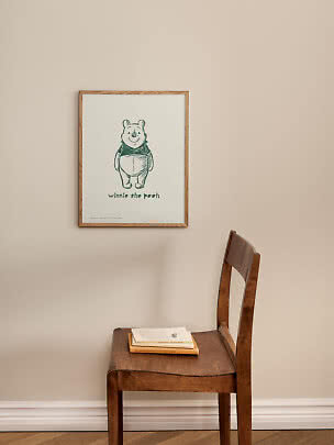 Gerahmtes Winnie Puuh Poster an beiger Wand über einem Holzstuhl mit Büchern