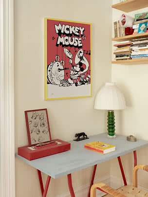 Mickey-Mouse-Poster im gelben Rahmen über grauem Tisch mit grüner Lampe und Büchern