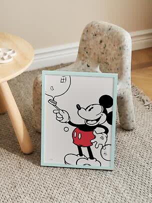 Gerahmtes Mickey-Mouse-Poster mit hellblauem Rahmen, an einen kleinen Stuhl auf Teppich gelehnt