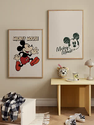 Two Mickey Mouse posters in light wooden frames above a small table in a children's room
