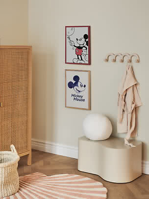 Camera per bambini con due poster di Topolino, ganci da parete, accappatoio beige e panca.