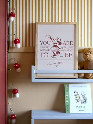 Gerahmtes Minnie-Mouse-Poster auf Regal neben Teddybär und Buch im Kinderzimmer
