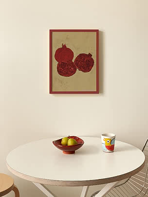 Affiche encadrée de grenades rouges au-dessus d’une table blanche avec coupe de fruits et tasse colorée