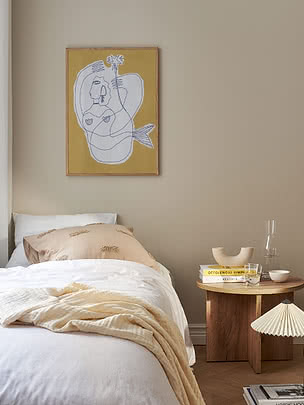 Schlafzimmer mit weißem Bett, Holznachttisch und gerahmtem gelbem Kunstdruck an beiger Wand