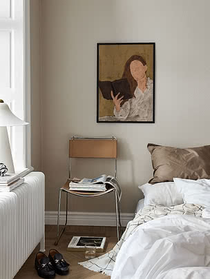 Dormitorio con cama, silla con revistas y cuadro enmarcado de una mujer leyendo en la pared