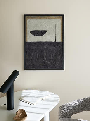 Ingelijste abstracte kunstprint in zwart, beige en wit aan de muur boven een witte tafel