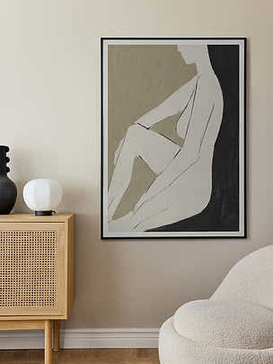 Framed abstract poster of a seated figure in beige, white and black on a wall