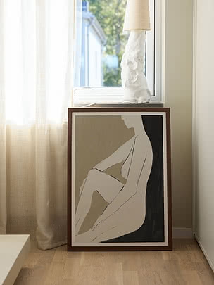 Framed abstract art print of a seated figure by a window with curtain and table lamp.