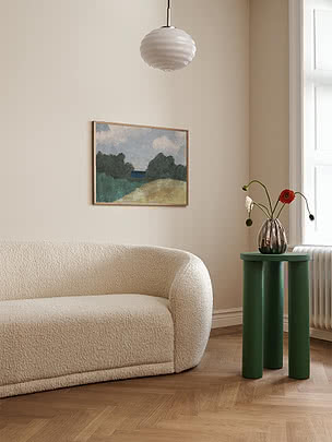 Grønt rundt sidebord ved cremefarvet sofa med vase, blomster og maleri i lyst rum