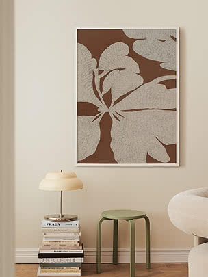 Framed botanical art print in brown and beige on wall above books, lamp and green stool
