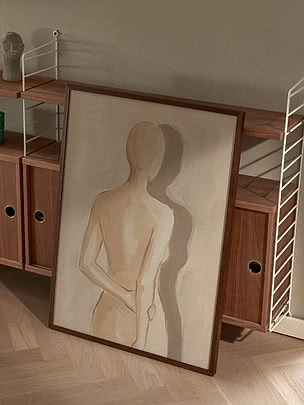Abstrakt målning av en stående figur i träram, lutad mot en valnötsfärgad hylla.