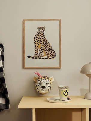 Inramad poster med stiliserad gepard på beige vägg ovanför ljust bord
