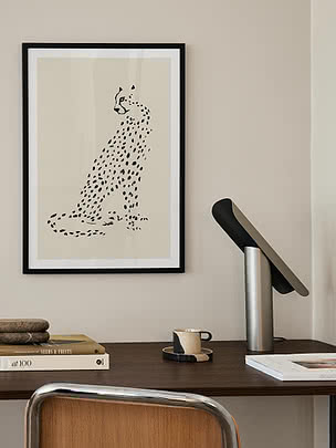 Indrammet plakat med en siddende plettet stor kat over et skrivebord med bøger og en metallampe