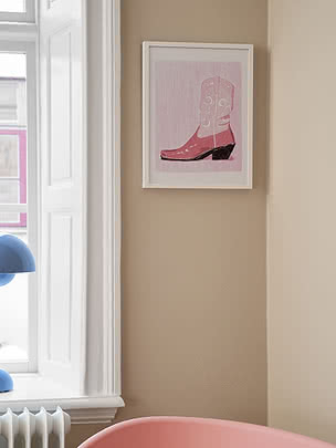 Gerahmter Kunstdruck mit rosa Cowboystiefel an beiger Wand neben einem Fenster