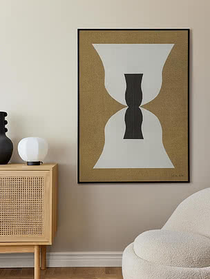 Abstrakt plakat i sort ramme over en rattan-kommode med bordlampe