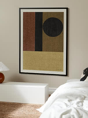 Geometrisk plakat i sort ramme over en hvid bænk i et soveværelse