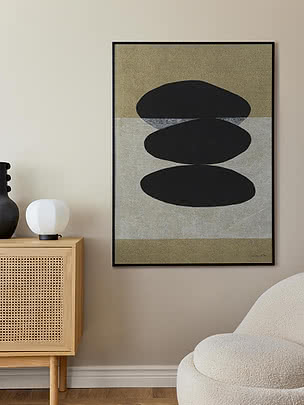 Abstraktes Poster im schwarzen Rahmen neben einem Rattan-Sideboard und einem Bouclé-Sessel